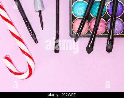 Weihnachten Make-up Kosmetik. Helle farbe Glitzer Lidschatten, schwarzer Eyeliner, Mascara, Lipgloss, Make up Pinsel und Applikator mit Zuckerstange auf Stockfoto
