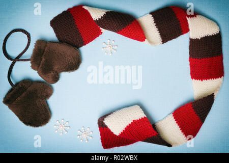 Zusammensetzung der kleine Pelz Fäustlinge, strickschal und kleine Schneeflocken auf Blau strukturierten Hintergrund. Cute winter Rahmen mit leeren Raum für Text Stockfoto
