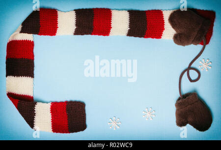 Zusammensetzung der kleine Pelz Fäustlinge, strickschal und kleine Schneeflocken auf Blau strukturierten Hintergrund. Cute winter Rahmen mit Kopie Raum Stockfoto