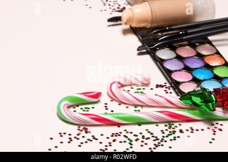 Nahaufnahme der Zuckerstangen mit Geschenkpapier Bögen umgeben von Konfetti auf dem Hintergrund der Make-up-Produkte und Zubehör. Christmas Party Make-up conce Stockfoto