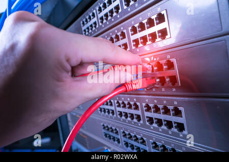 Hand, die Netzwerkkabel auf dem Switch Hub im Server raum Hintergrund Stockfoto