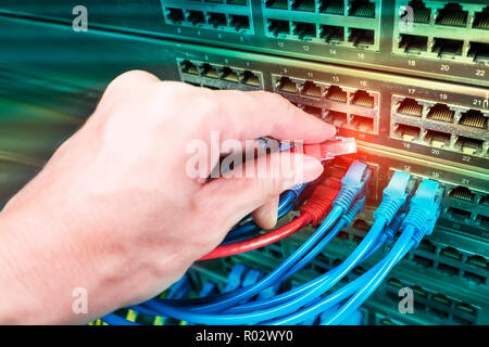 Hand, die Netzwerkkabel auf dem Switch Hub im Server raum Hintergrund Stockfoto