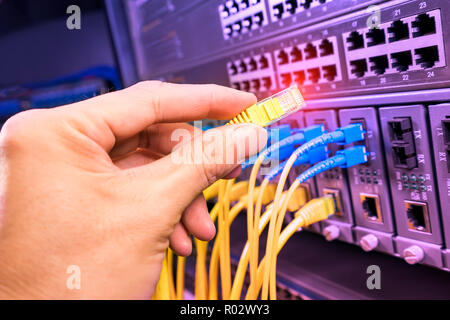 Hand, die Netzwerkkabel auf dem Switch Hub im Server raum Hintergrund Stockfoto