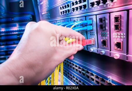 Hand, die Netzwerkkabel auf dem Switch Hub im Server raum Hintergrund Stockfoto