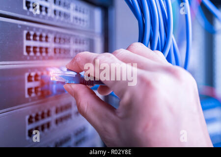 Hand, die Netzwerkkabel auf dem Switch Hub im Server raum Hintergrund Stockfoto