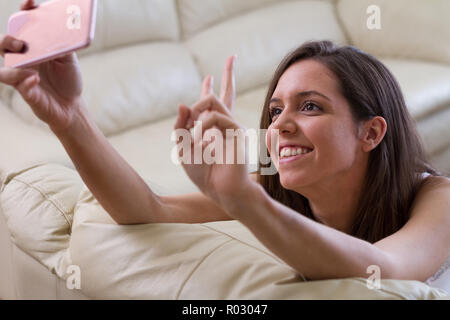 Hübsche brünette Mädchen, stützte sich auf ihren Arm lächelte ihr Mobiltelefon, mit dem Sie eine sehr helle und feminin selfie Foto suchen Stockfoto