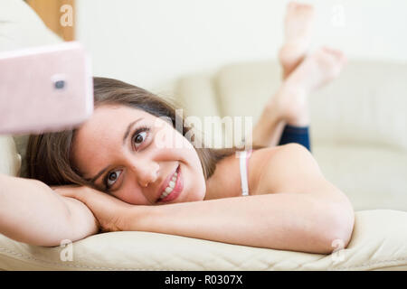 Hübsche junge brunette kaukasische Frau ruht auf der Couch, während eine selfie mit Überraschung Überraschung Gesicht und Gesicht der Überraschung und Unsicherheit, wi Stockfoto