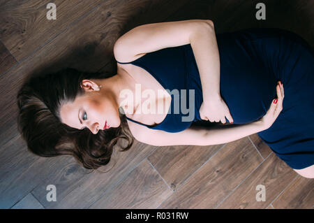 Schwangere Frau im blauen Kleid am Boden liegt Stockfoto