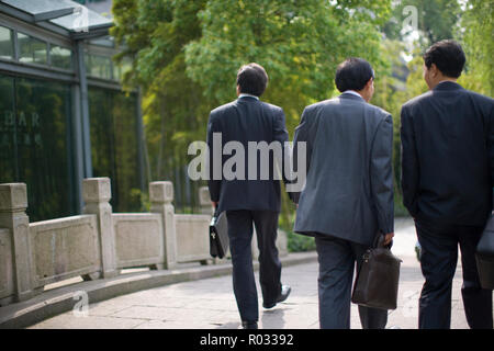 Drei Geschäftsleute gehen Seite an Seite über eine gepflasterte Brücke. Stockfoto