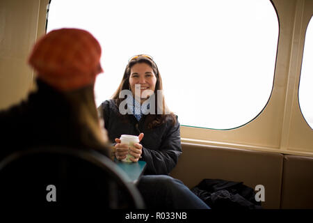 Junge Frau sitzt im Ferry mit Freundin Kaffee trinken und lachen Stockfoto
