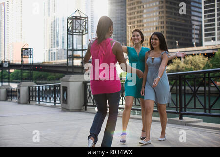 Zwei lächelnde Freunde ihre Arme ausstrecken zu umarmen, einen anderen Freund in der Stadt. Stockfoto
