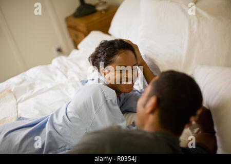 Lachende junge Frau liegen auf einem Bett mit ihrem Freund in Ihrem Schlafzimmer. Stockfoto