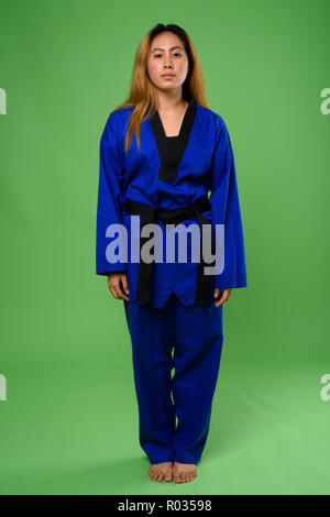 Junge asiatische Frau trägt blaue Karate Gi gegen grüne backgroun Stockfoto