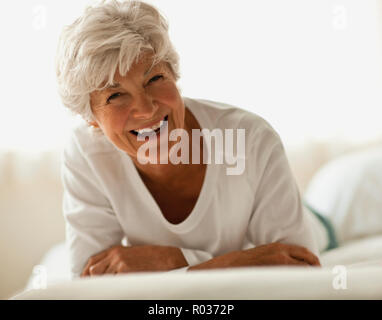 Lächelnd senior Frau liegt auf auf ihren vorderen in einem Bett. Stockfoto