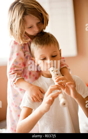 Junge spielt der Recorder, mit seiner Schwester ihn mit einer Umarmung. Stockfoto