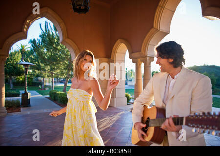 Lächelnd Mitte erwachsenen Mann spielt eine akustische Gitarre, während sein Partner auf aussieht. Stockfoto