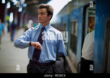 Geschäftsmann prüft den Zeitpunkt auf seine Armbanduhr, wie er in einem Bahnhof wartet. Stockfoto