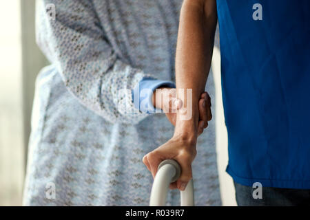 Krankenschwester unterstützt das Handgelenk der jungen männlichen Patienten als Er lernt wieder laufen. Stockfoto