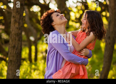 Lachen Mitte der erwachsenen Frau ihre Tochter, als sie gemeinsam in einem Wald stehen. Stockfoto