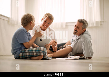Vater und seine zwei Söhne sitzen auf dem Boden, der eine digitale Tafel. Stockfoto