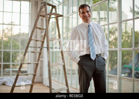 Mitte der erwachsenen Geschäftsmann stehend die Hände in den Taschen und lächelnd. Stockfoto