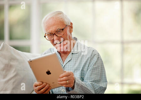 Gerne älterer Mann Spaß suchen an einem digitalen Tablet beim Tragen Schlafanzug. Stockfoto