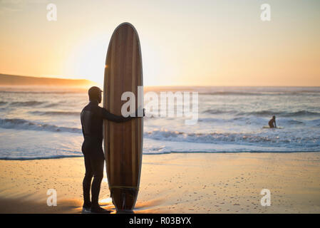 Mitte der erwachsene Mann mit einem Surfbrett am Strand. Stockfoto