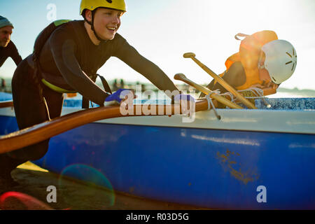 Lächelnd Teenager in einem Helm und Neoprenanzug aus seinem Kanu drückt am Strand. Stockfoto