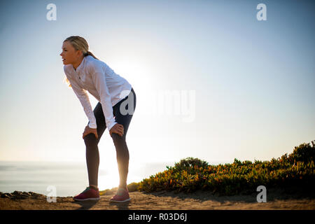 Junge Frau nimmt einen Bruch von ihrer Sonnenaufgang Joggen entlang der Klippen der Blick auf den Ozean zu bewundern. Stockfoto