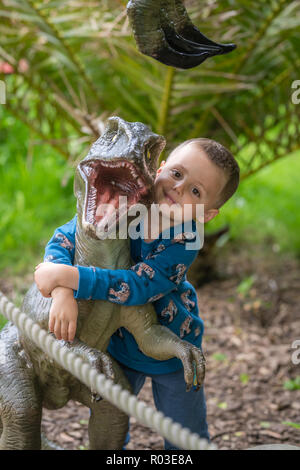 Kleinen Niedlichen kaukasischen Jungen umarmen kleine Raptor replica Abbildung in einem Freizeitpark Stockfoto