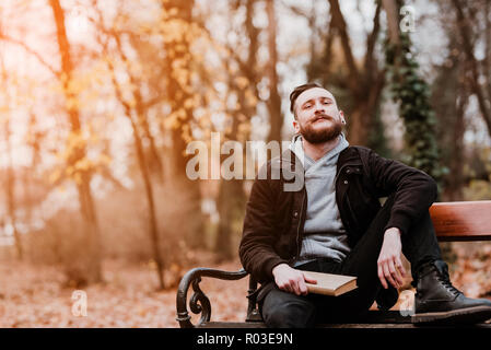Retro Style Foto einer jungen hipster Mann sitzt auf einer Bank mit einem Buch und Träumen. Stockfoto