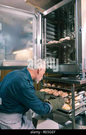Inhaber der Bäckerei, Croissants in Backofen Arbeiten am Morgen Stockfoto