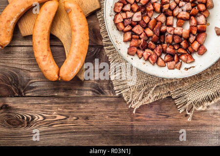 Gebratene Würstchen in Scheiben in einem Würfel auf einer Pfanne auf einem hölzernen Hintergrund. Stockfoto