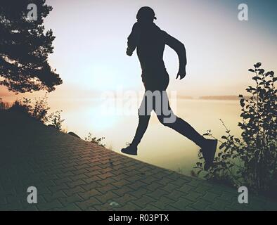 Freeze Action Shot von hohen laufenden Sportler tragen trendige Sportschuhe und Sportbekleidung morgens trainieren am Ufer. Pavement Titel rund um den See. Stockfoto