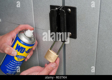 Kaukasische Mann Spritzen einer Aerosoldose WD-40 Schmiermittel auf ein Metall Vorhängeschloss, Großbritannien Stockfoto