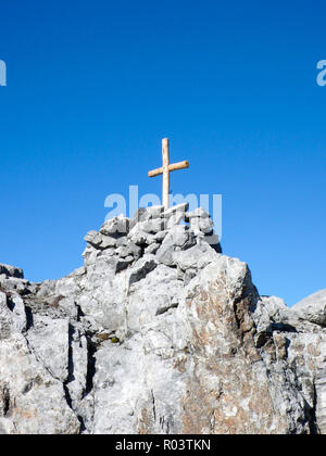 Isolierte hölzernen Gipfelkreuz auf einem scharfen und gezackten Gipfel unter einem blauen Himmel Stockfoto