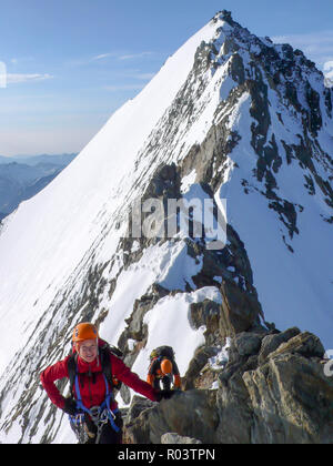 Männliche und weibliche Bergsteiger auf einem ausgesetzten felsigen Gipfelgrat auf ihrer Weise zu einer hochalpinen Gipfel Stockfoto