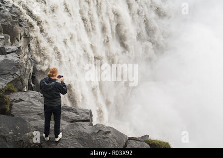 DETTIFOSS, ISLAND - AUGUST 2018: Mann in Schwarz, der Wasserfall auf der Steilküste Vatnayokull National Park. Stockfoto