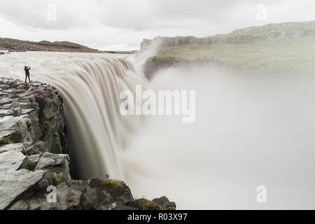 Menschliche Figur stehend auf der Klippe neben dem Wasserfall Dettifoss in Vatnayokull National Park, Island. Bewölkten Tag, langen Belichtungszeit. Stockfoto