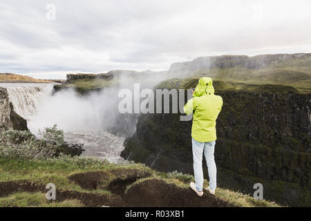 DETTIFOSS, ISLAND - AUGUST 2018: Mann in Grün Regenmantel, der Wasserfall auf der Steilküste Vatnayokull National Park. Stockfoto