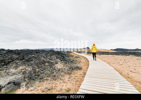 Frau im gelben Regenmantel wandern in Krafla Vulkan Lava Feld um Leirhnjukur Berg, Island. Stockfoto