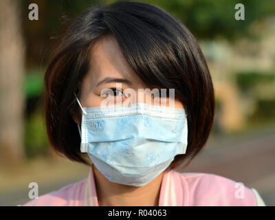 Junge Taiwanese Frau mit schönen orientalischen Augen trägt ein hell-blau Einmal-OP-ohrläppchen Gesichtsmaske. Stockfoto