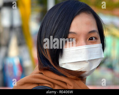 Junge Taiwanese Frau mit großen Augen trägt in der Öffentlichkeit ein weißes Einmal-OP-ohrläppchen Gesichtsmaske. Stockfoto