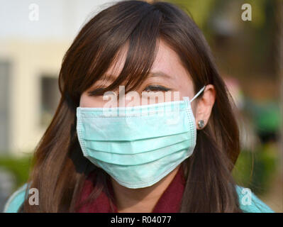 Junge Taiwanese Frau mit orientalischen Augen trägt ein hell-grün Einmal-OP-ohrläppchen Gesichtsmaske. Stockfoto