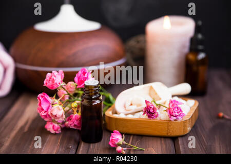Spa noch Leben mit Rose ätherisches Öl Flasche, Badesalz, Kerze und Aromatherapie Diffusor, innen Holz spa Einstellung Stockfoto