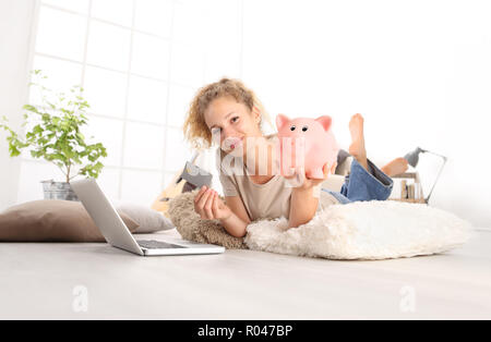 Junge Frau mit Kreditkarte und Sparschwein mit Laptop Computer. Online shopping Konzept speichern, Liegen auf Wohnzimmer Holzboden in modernen whit Stockfoto