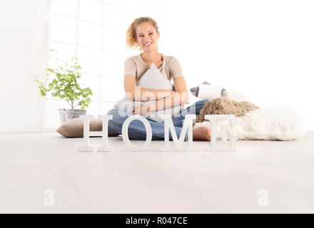 Home Konzepte, junge Frau umarmt eine grosse bequeme Kissen, sitzend auf dem Holzboden eines modernen Wohnzimmer mit Startseite Text, kopieren Raum Vorlage Stockfoto