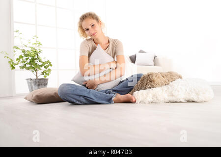 Home Konzepte, junge Frau umarmt eine grosse bequeme Kissen, sitzend auf dem Holzboden eines modernen Wohnzimmer, Raum Vorlage kopieren Stockfoto