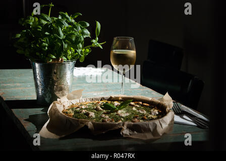 Pizza mit Lachs, ein Glas Weißwein und Basilikum in der Dunkelheit Stockfoto