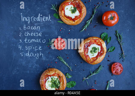 Drei hausgemachten Mini Pizza mit Tomaten, Käse und Speck, Verletzungen und Gewürze auf einem dunklen Hintergrund mit einer schriftlichen Rezept. Stockfoto